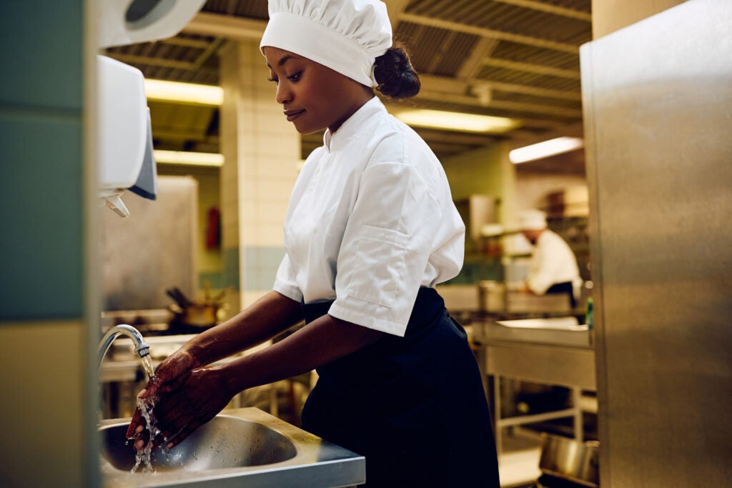 Women chef washing her hands in the kitchen sink to help foster a culture of food safety in their food service operation.