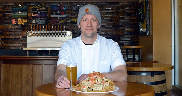 Chef Chris VanderMeer sits at a table with a plate of Duck Confit Nachos