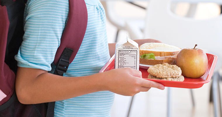 A student carries a Community Eligibility Provision lunch on a red tray.