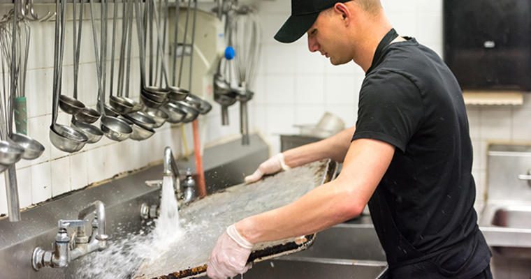 Worker washing large tray in commercial kitchen