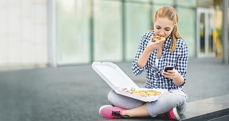 Woman eating pizza looking at phone
