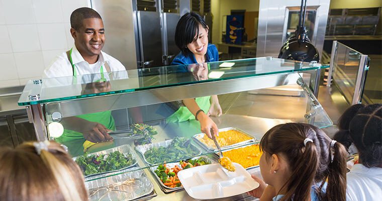 Education food service workers serve elementary school students at a salad bar.