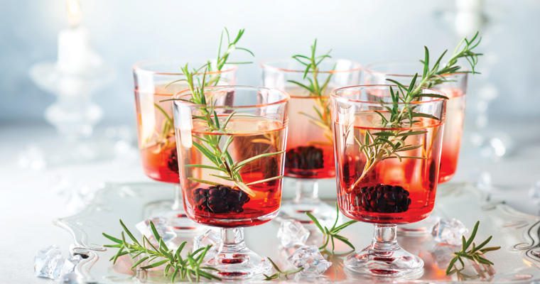 Five festive glasses filled with holiday drinks and an herbal garnish