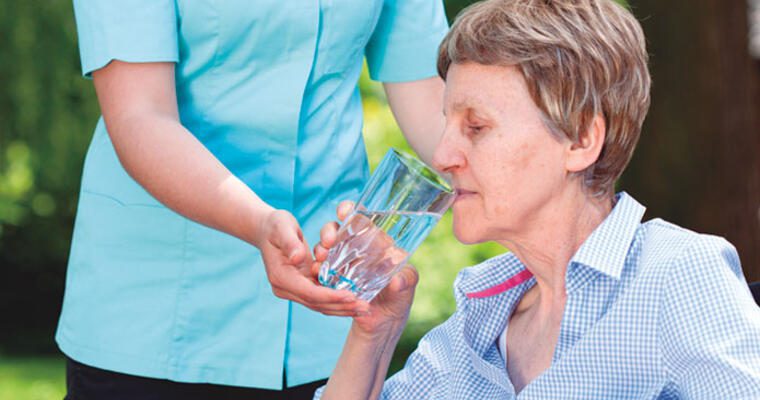 Older woman drinking water with assistance