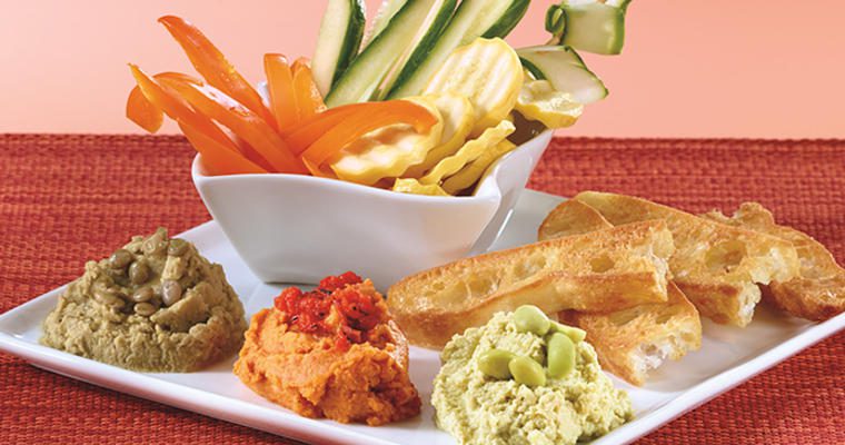 Three types of hummus with bread and sliced vegetables
