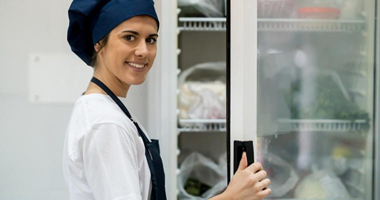 Woman in healthcare kitchen opening cooler door to take inventory
