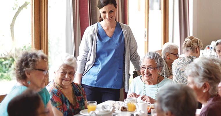 Server talks to seniors at a nursing home dining table