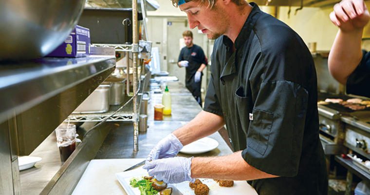 Millennial kitchen worker cutting food at a prep station