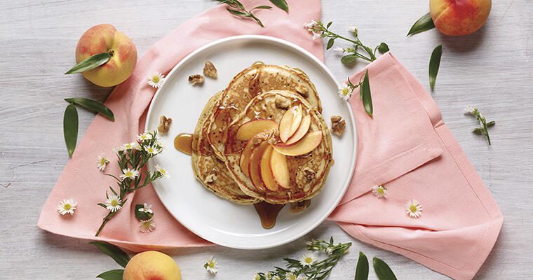 Fluffy pancakes and peaches on a white plate with pink napkins.