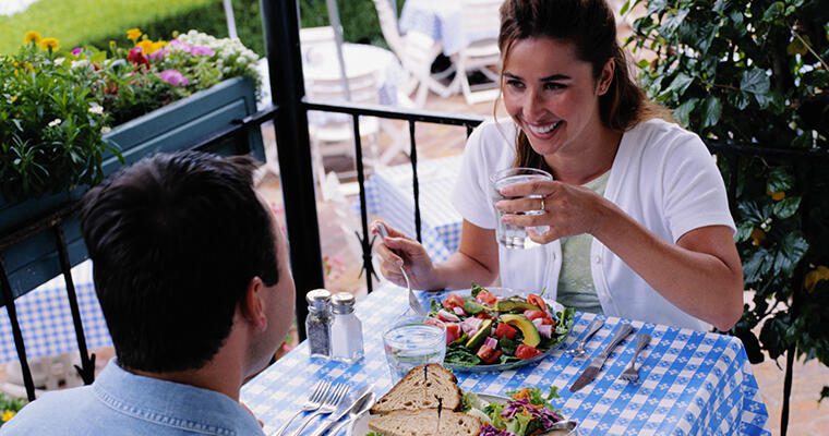 A man and a woman enjoy salads and sandwiches at a restaurant patio dining table.