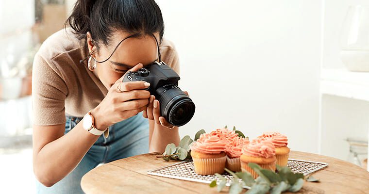 A photographer leans in for a close-up image of cupcakes on a placemat.