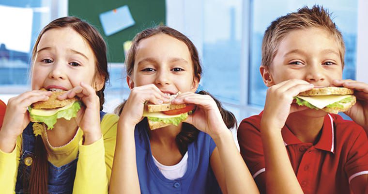 Kids munching on sandwiches at a school dining room