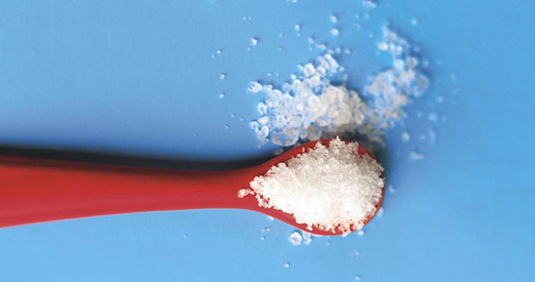 Red measuring spoon of salt on blue background