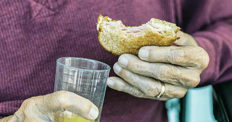 Man holding sandwich with a bite taken out and drinking glass