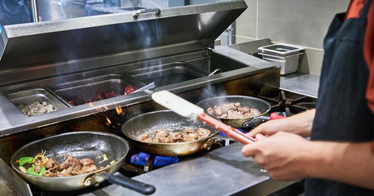 Chef cooking meat in three pans