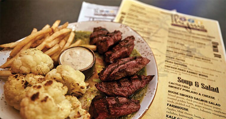 Steak, fries, and cauliflower on plate with menu in the background
