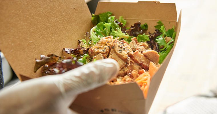 Gloved hand holding takeout box with chicken and lettuce