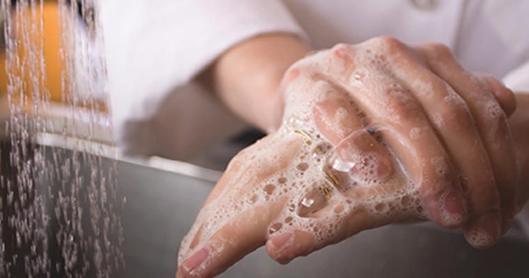 Hands with soap suds being scrubbed under a running faucet