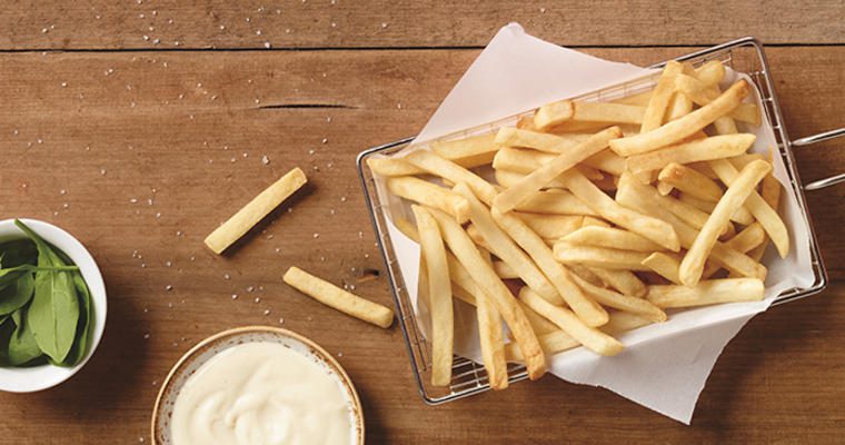 a basket of fries and condiments on a wooden tabletop