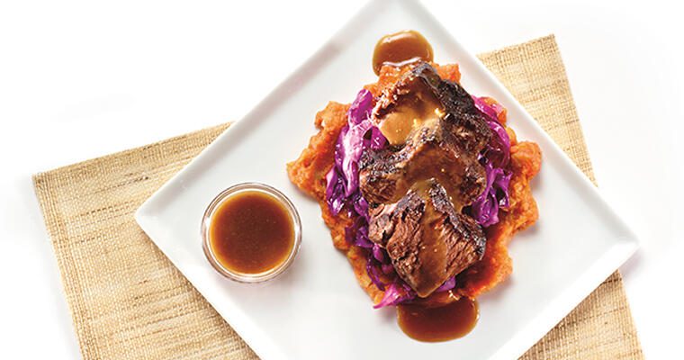 Beef rib sauerbraten and a ramekin of gravy on a square white plate.