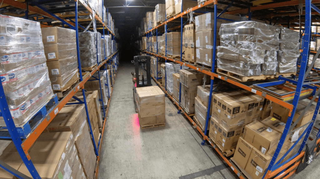 Pallets stacked on shelves with a forklift lifting a pallet in the distribution center in Miami, FL.