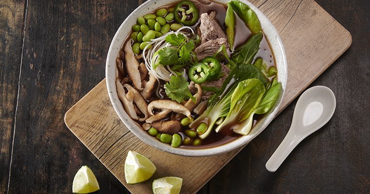 Beef and vegetable pho in a white bowl