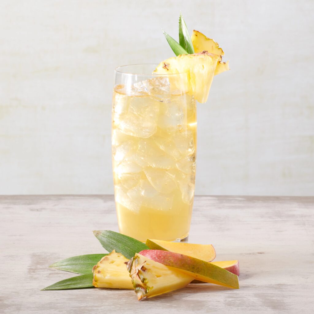 a tall glass filled with a drink next to a sliced pineapple and apple.