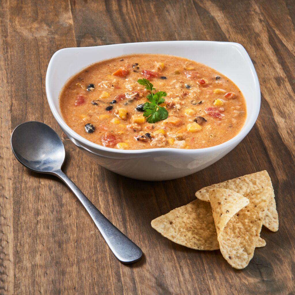 a bowl of chicken enchilada soup with a spoon and handful of tortilla chips beside it