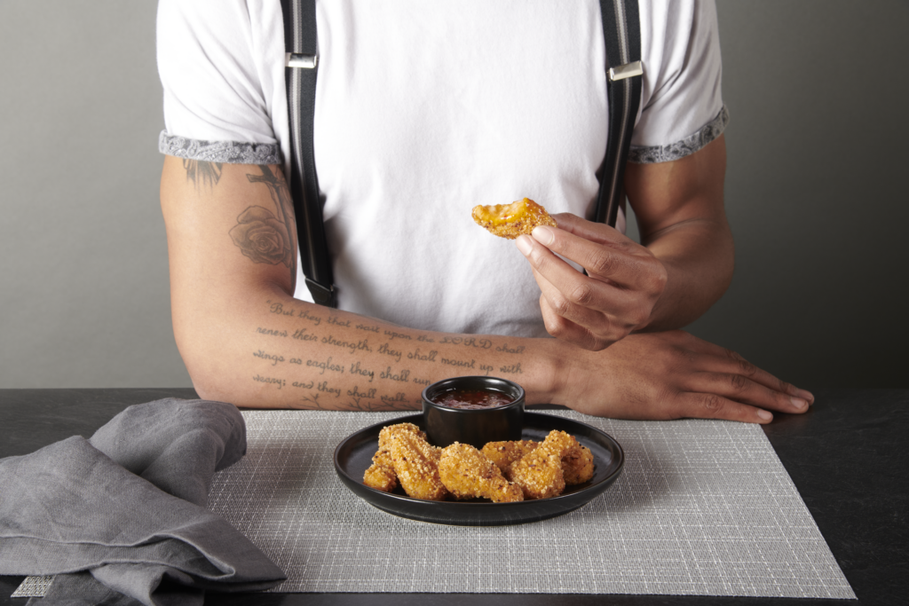 a man taking a bite out of plant based cauliflower wings