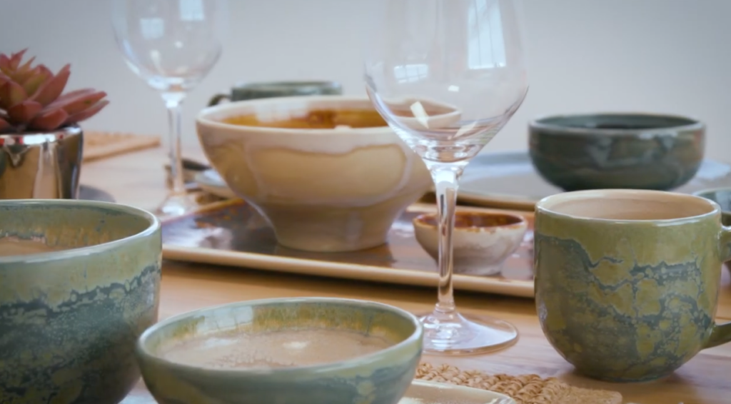 A variety of textured, hand-made restaurant dinnerware pieces with clear wine glasses in the middle