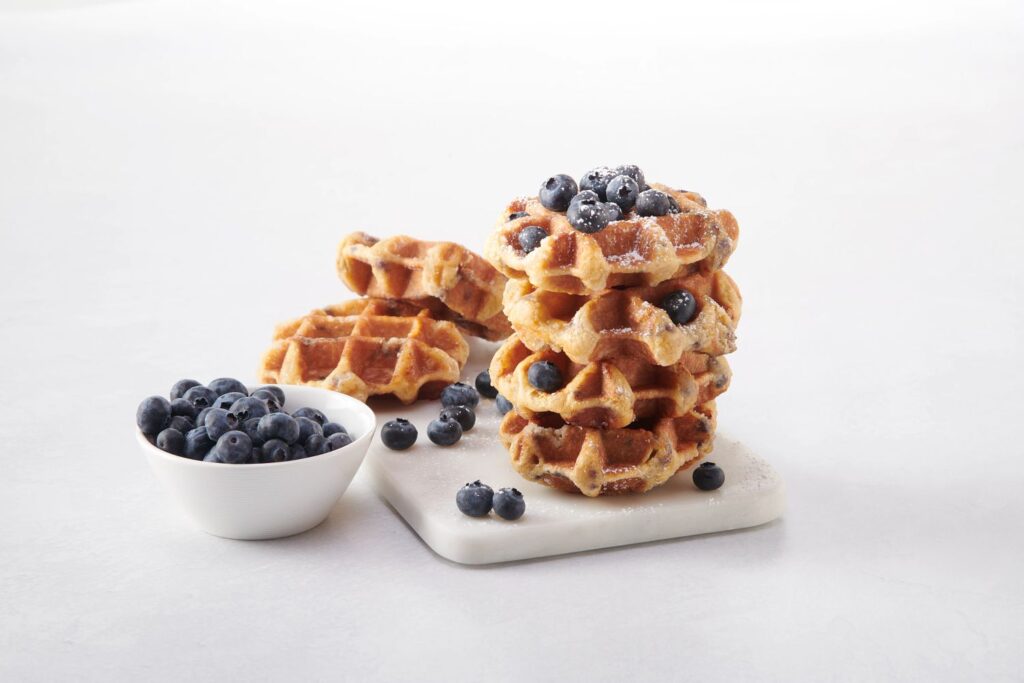  A stack of waffles covered in fresh blueberries.