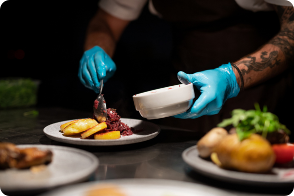 Chef wearing blue food safe gloves plating food on a white plate prepping for service. Austin Trends Event | Nice to Meet You