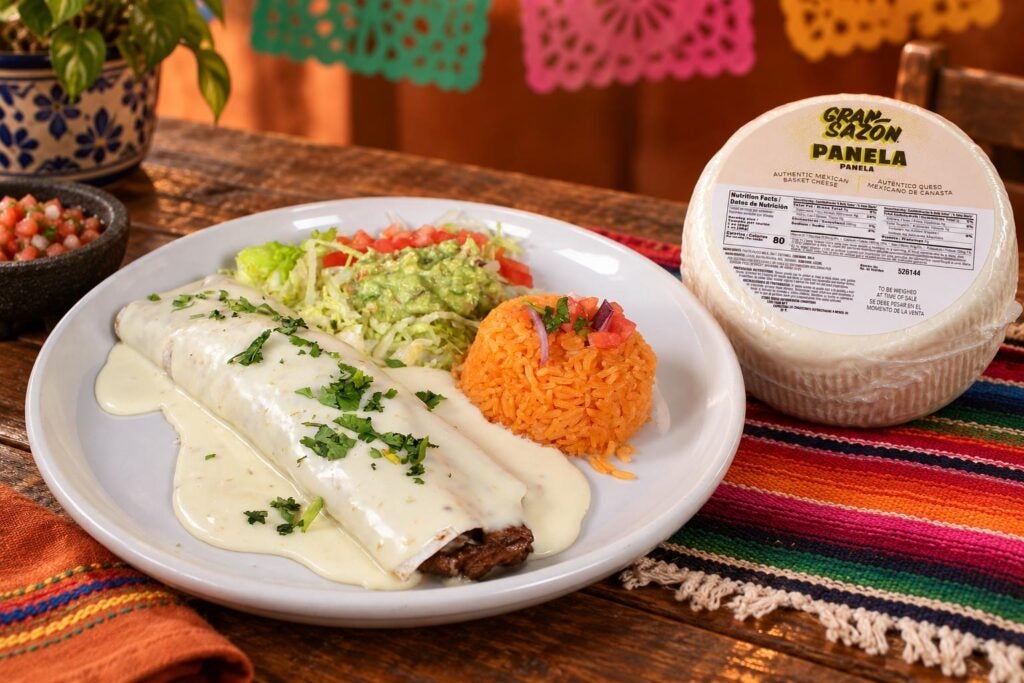 A smothered burrito served with rice, guacamole, and lettuce next to a wheel of Gran Sazón Panela basket cheese.