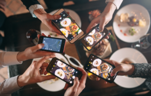 Top-down view of people holding smartphones to photograph dishes on a restaurant dining table.